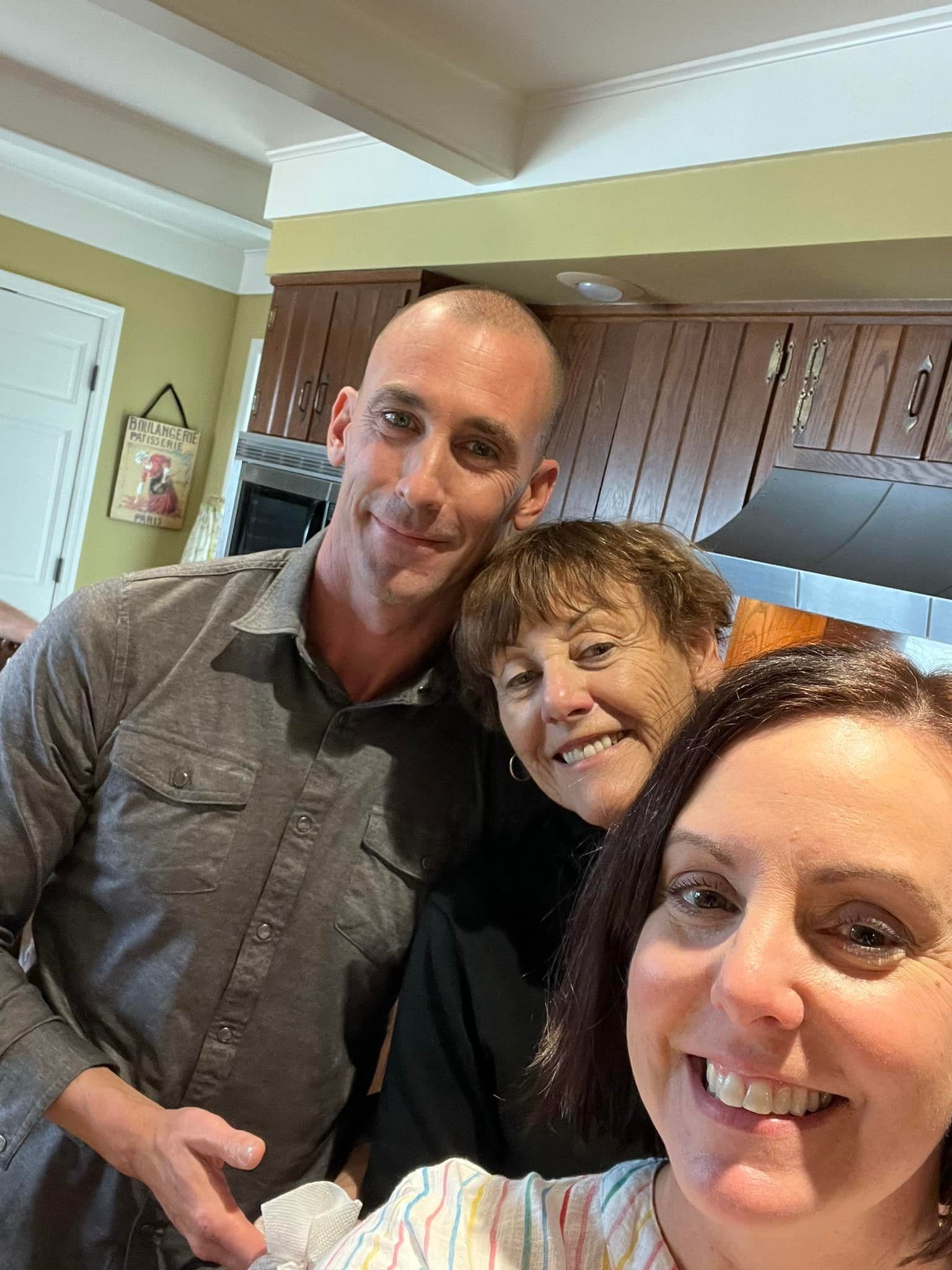 Three people smiling in a kitchen, with cabinets and a window in the background.