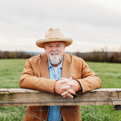 Smiling man in a straw hat leaning on a wooden fence in a grassy field