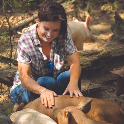Woman crouches petting a tan dog outdoors in dappled sunlight