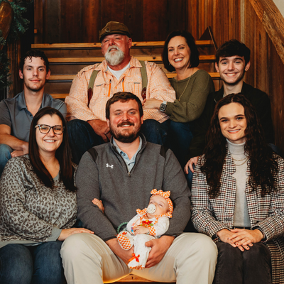 Six people pose indoors on a wooden staircase, smiling with a baby in the front.