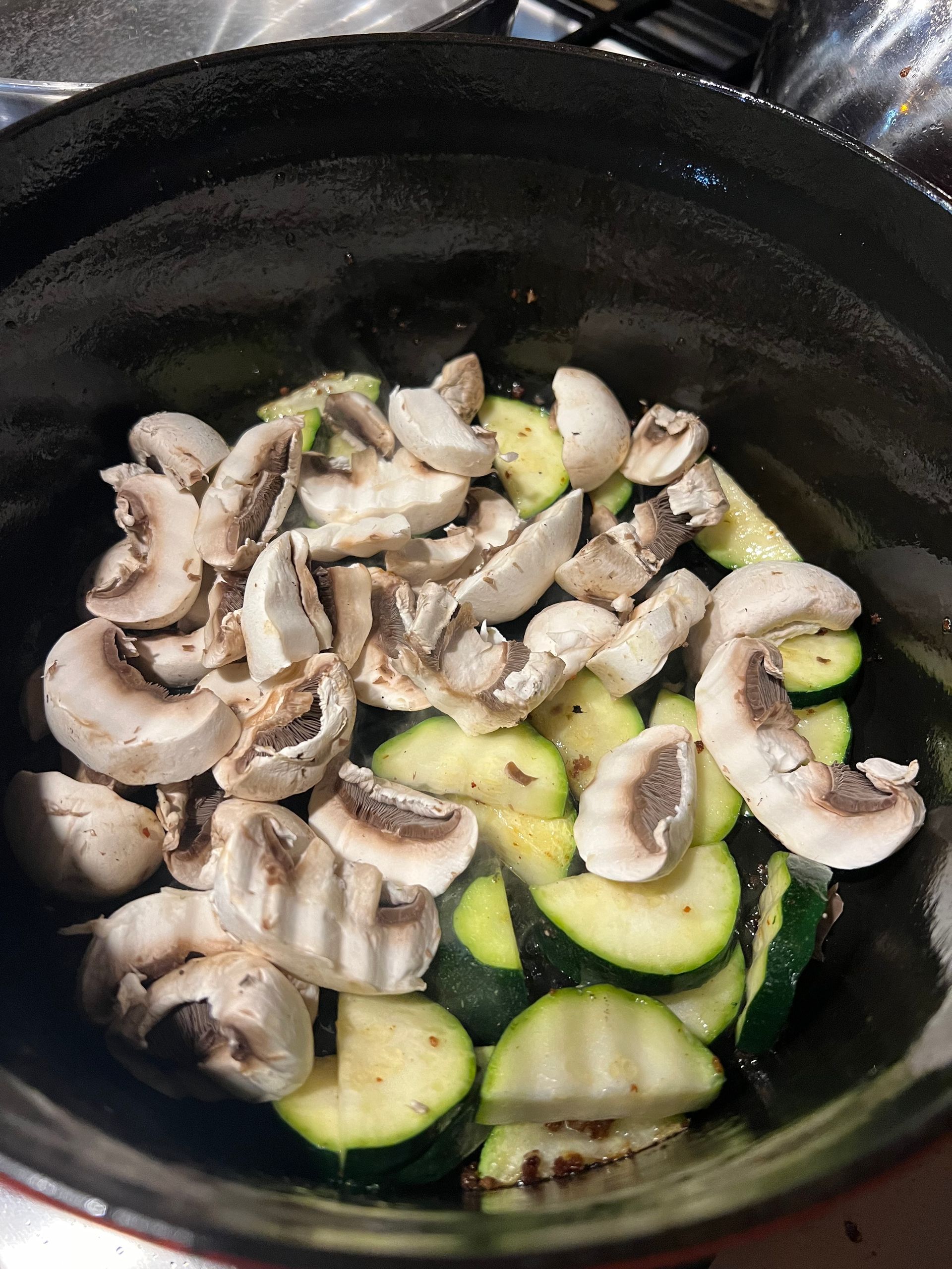 Sliced mushrooms and zucchini in a black skillet, lightly sautéing.