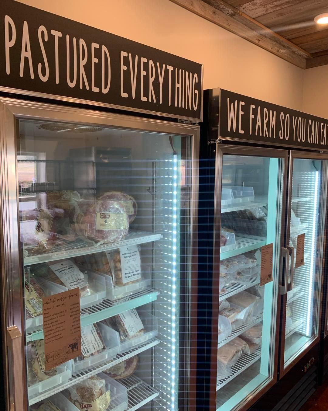 Refrigerated display cases with pasture-raised products in a store, topped by signs reading “PASTURED EVERYTHING.”