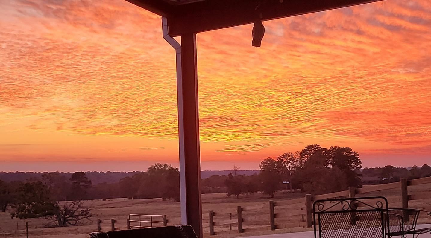 Sunset over a rural field with orange-pink sky, silhouetted porch posts, and distant trees