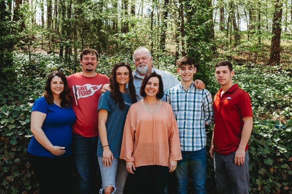 Six people standing together in a forest, smiling at the camera.