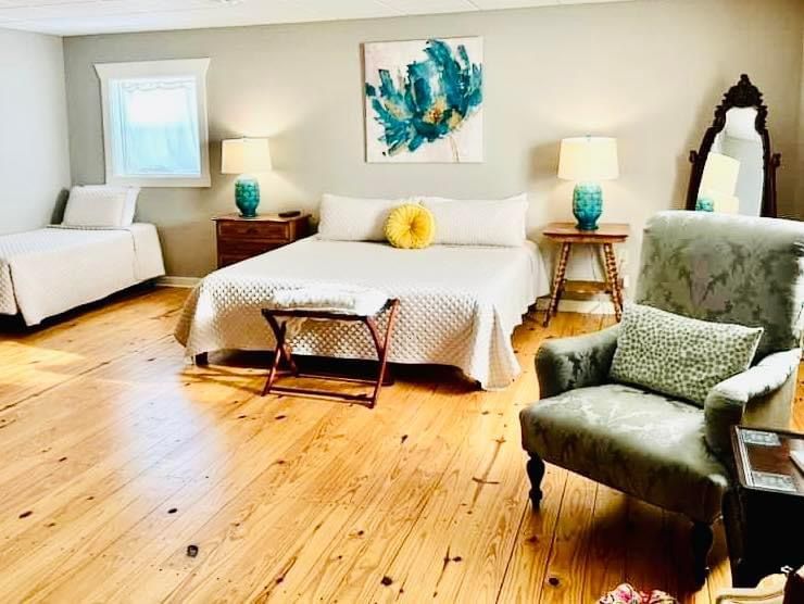 Bright bedroom with white bedding, green armchair, wood floors, and teal accents