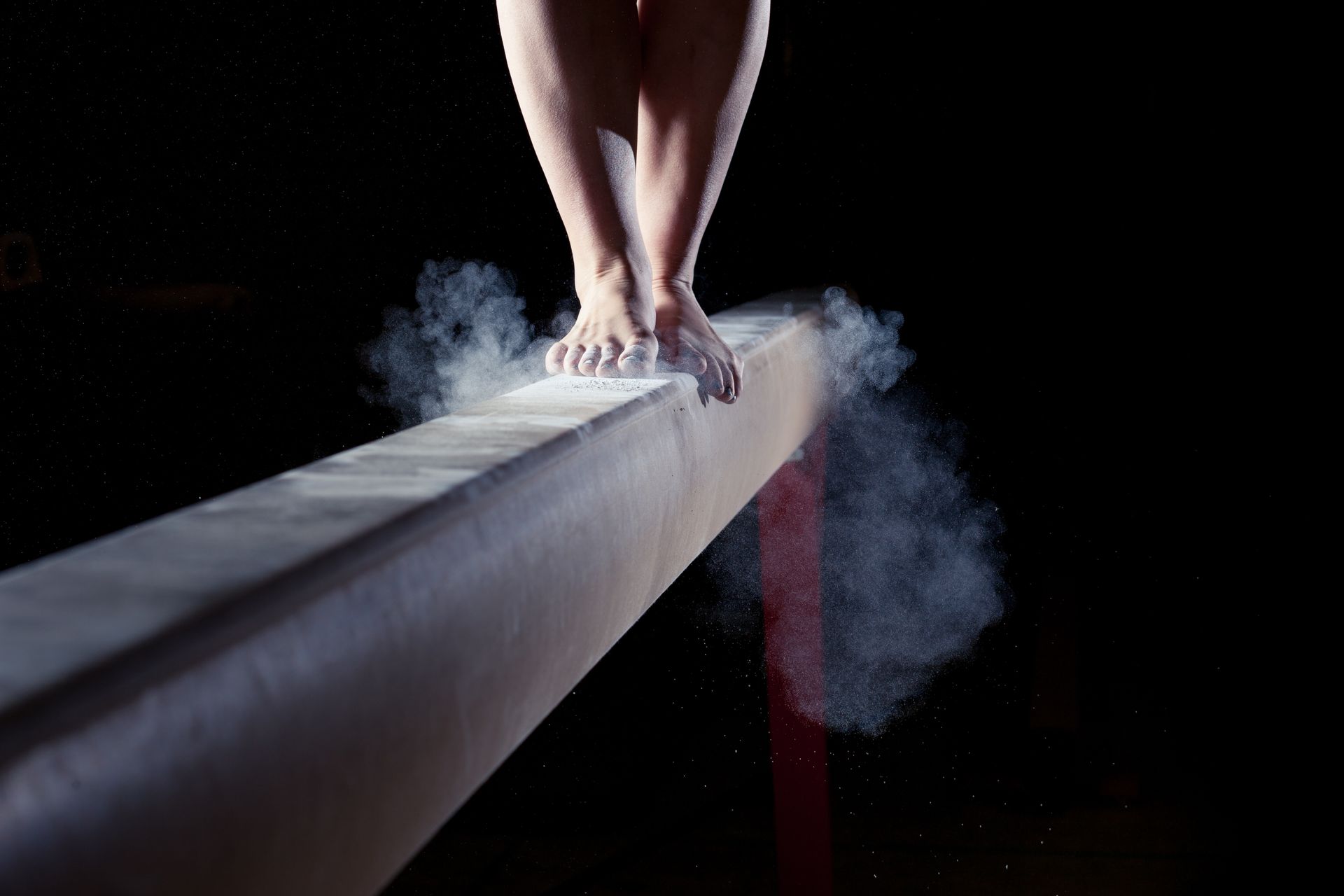 A girls feet on the beam in a dark gym with chalk dust