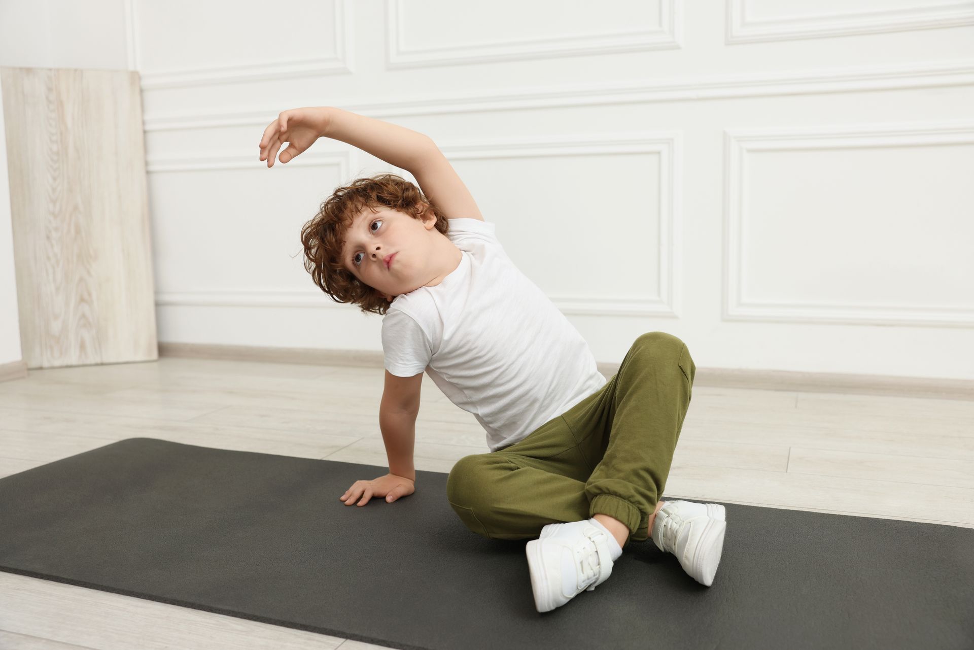 A young boy is doing stretches on the floor in a gym.