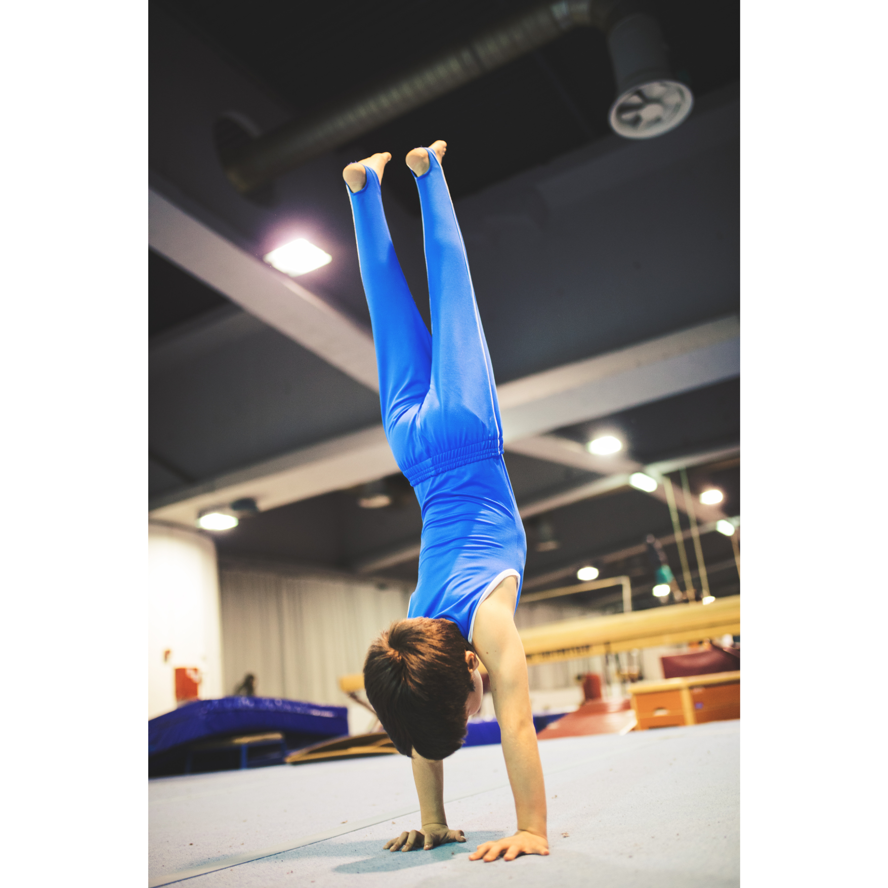 A man is watching a gymnast do a trick on rings in a gym.