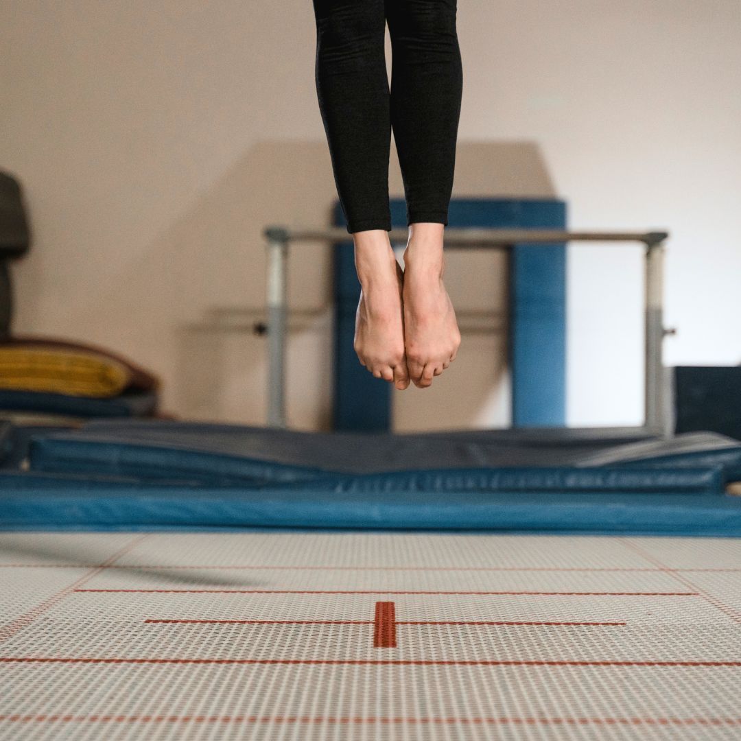 A young girl is sitting on a balance beam in a gym.