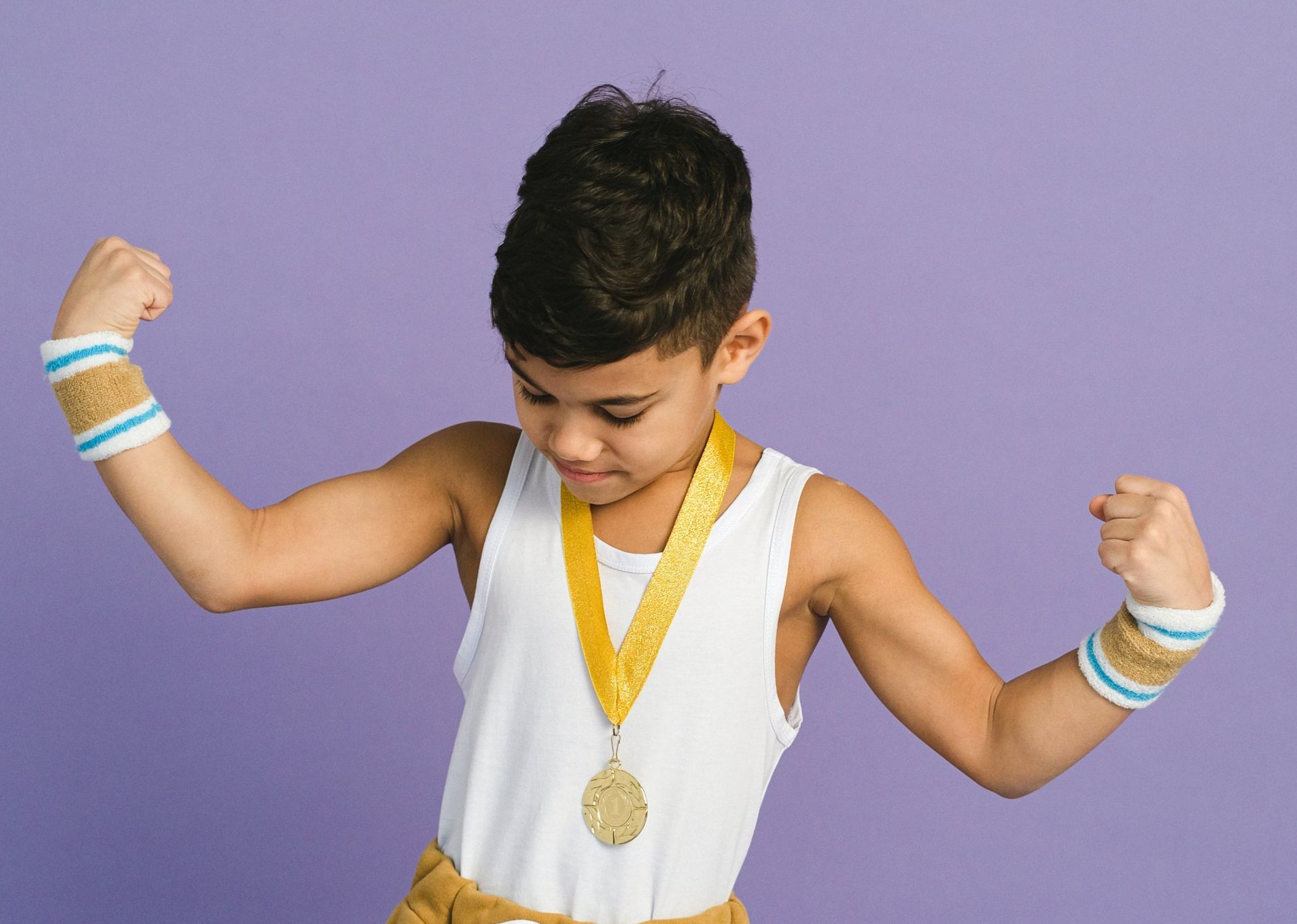 A young boy with a medal around his neck is flexing his muscles.