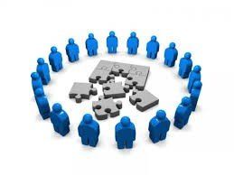 A group of blue people are standing in a circle around a puzzle.