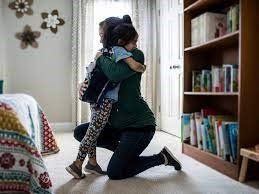A man is kneeling down and hugging a little girl in a bedroom.