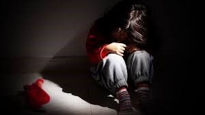 A young girl is sitting on the floor in a dark room.