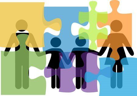 A group of people are holding hands in front of puzzle pieces.
