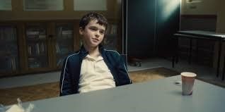 A young boy is sitting at a table with a cup of coffee.