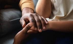 A person is holding another person 's hand while sitting on a couch.