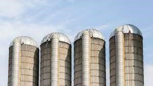 Four silos are lined up in a row against a blue sky.