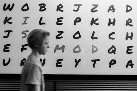 A boy is standing in front of a white board with letters on it.