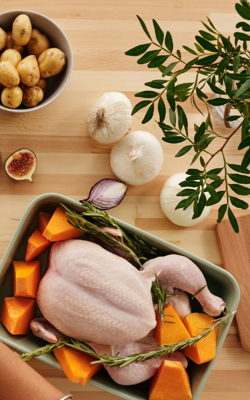 Raw chicken in a roasting pan with squash, rosemary, garlic, onions, and potatoes, ready for cooking.