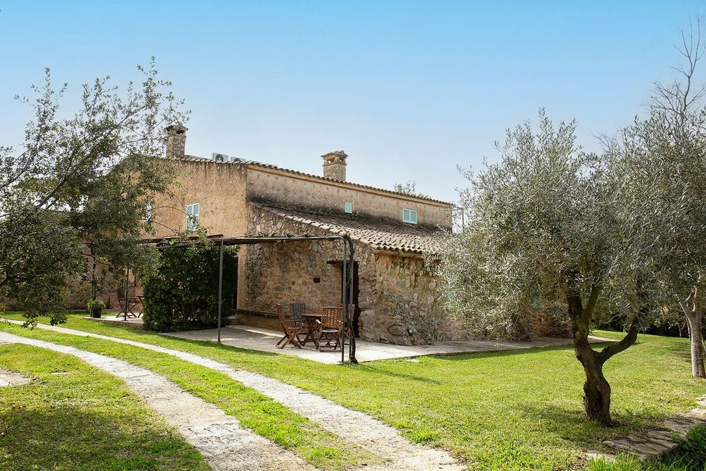 Casa de piedra con olivos y camino de grava bajo un cielo azul.