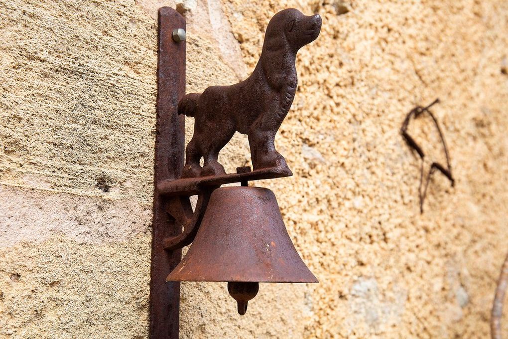Campana de metal oxidado con forma de perro montada en una pared de piedra texturizada.