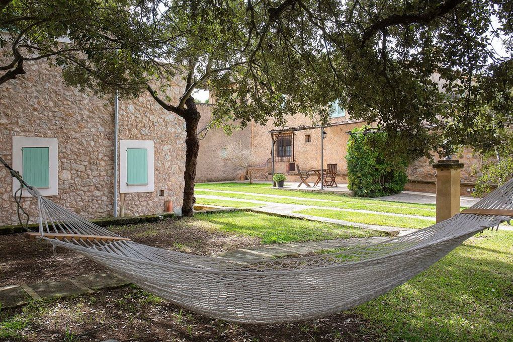 Hamaca en un patio con césped, edificio de piedra al fondo, debajo de un árbol.
