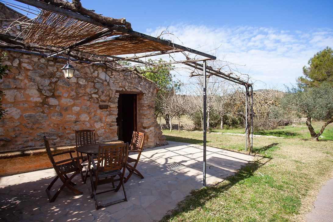 A stone building with a table and chairs under a pergola.
