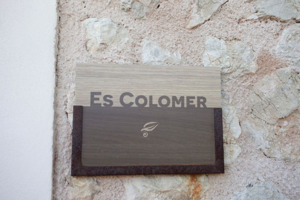 Un cartel de madera en una pared de piedra dice es colomer.