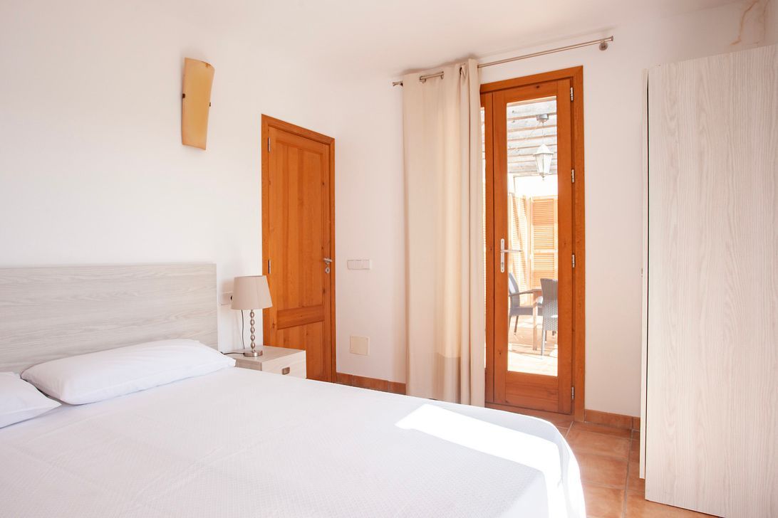 Ein Schlafzimmer mit Bett, Nachttisch, Lampe und Tür zum Balkon.