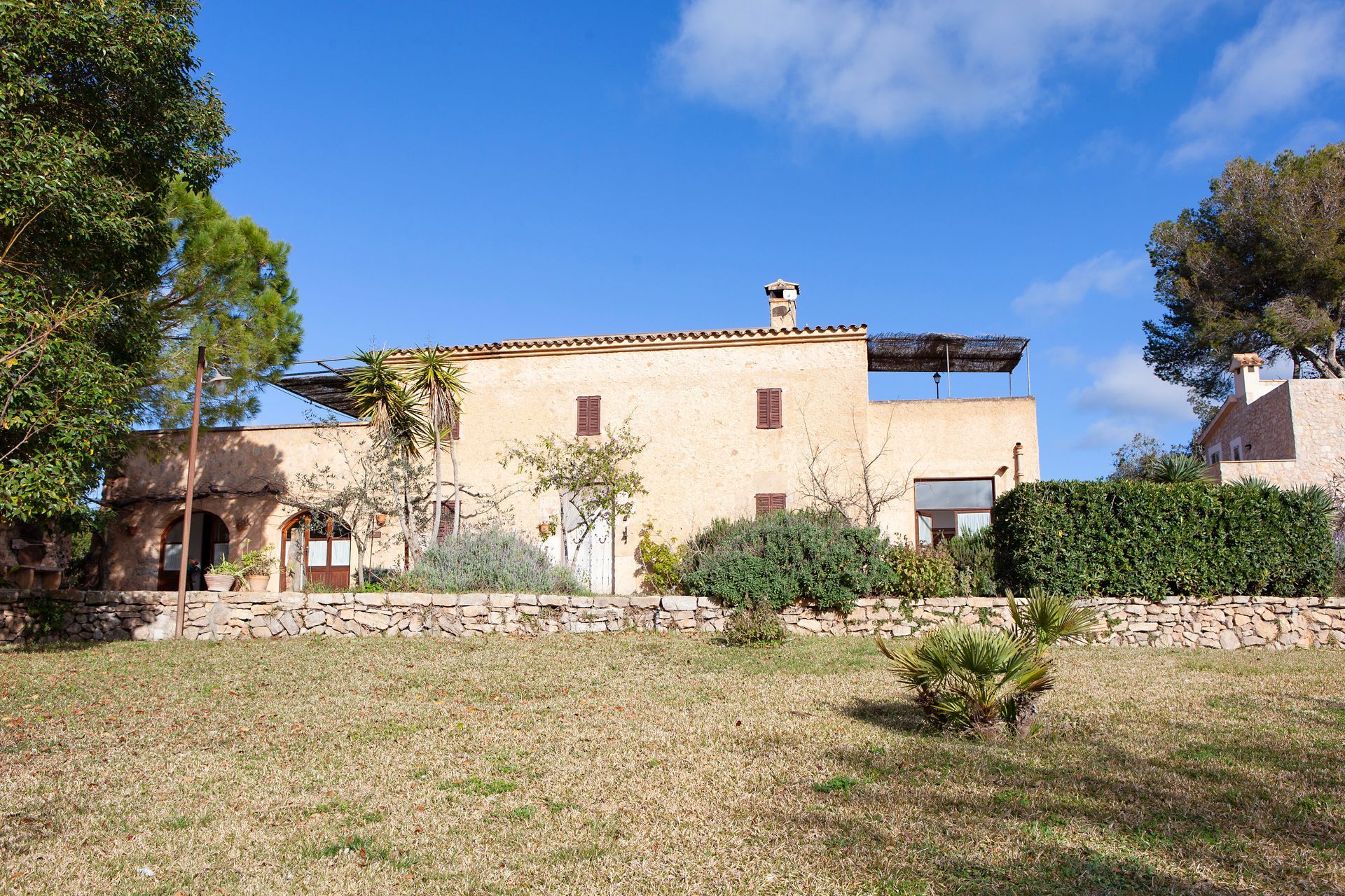 Una casa grande está rodeada de árboles y un muro de piedra.