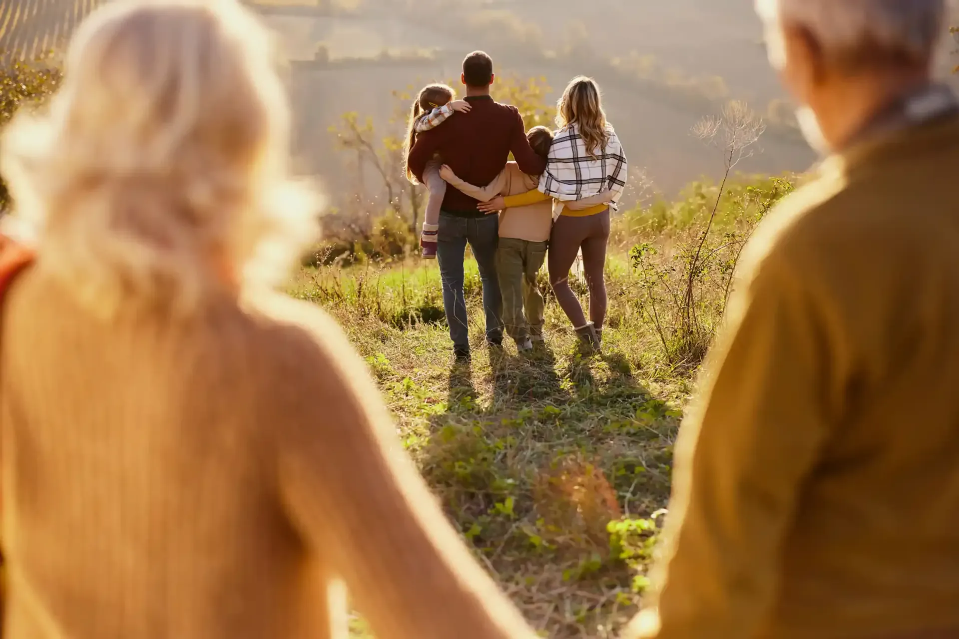 Family walking together on a sunny hillside, grandparents in foreground.