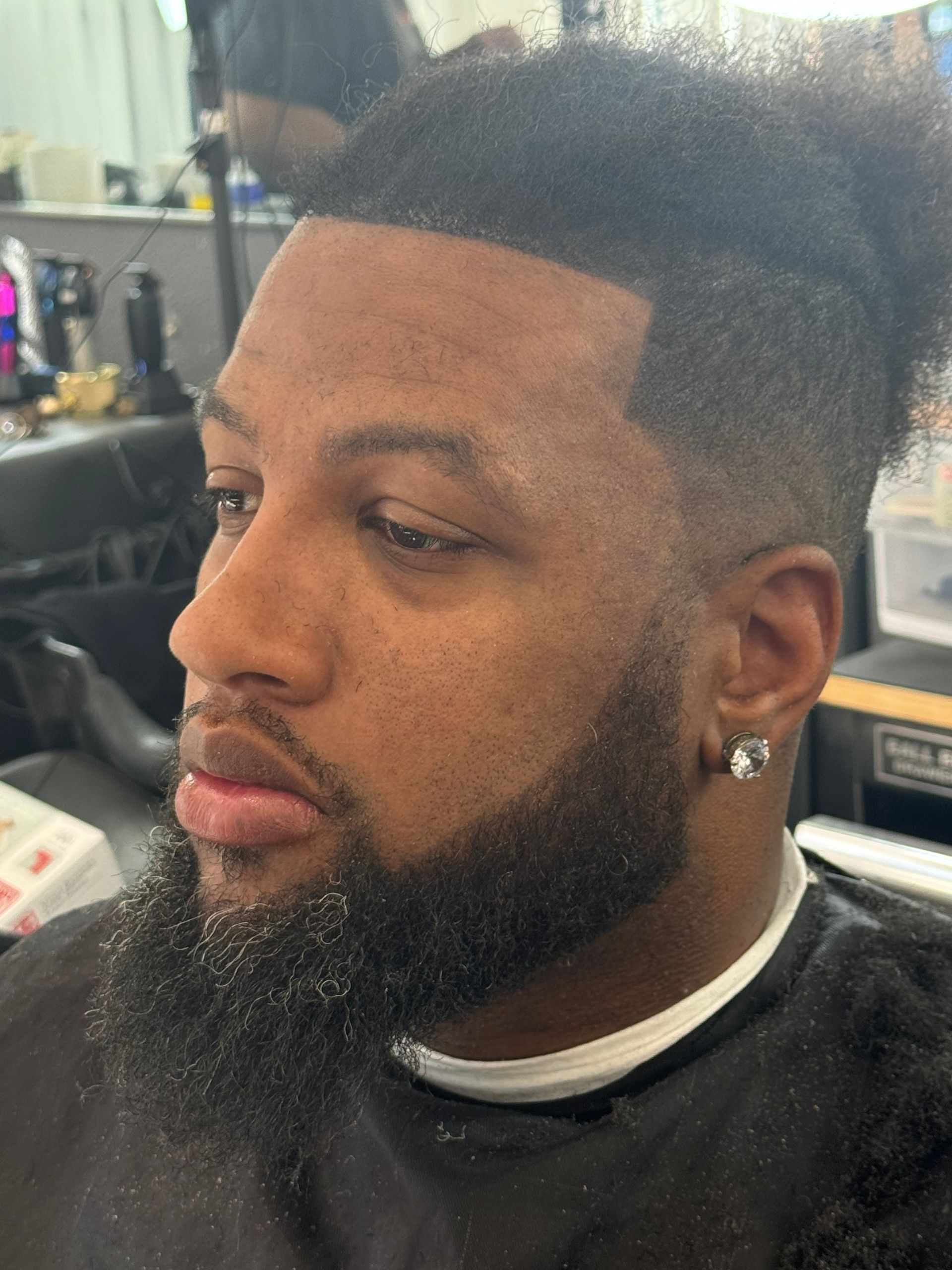 A man with a beard is getting his hair cut at a barber shop.