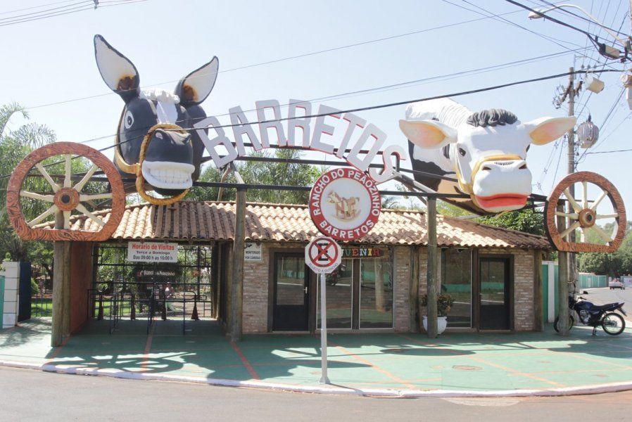 Entrada de Barretos com cabeças de vaca e burro, rodas de carroça e fachada de edifício.