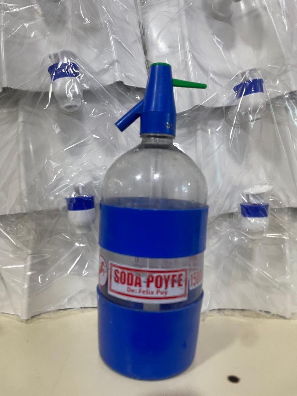 Encimera de cocina compacta con dispensador de agua, botellas azules, armarios de pared y una ventana con bolsas colgantes.