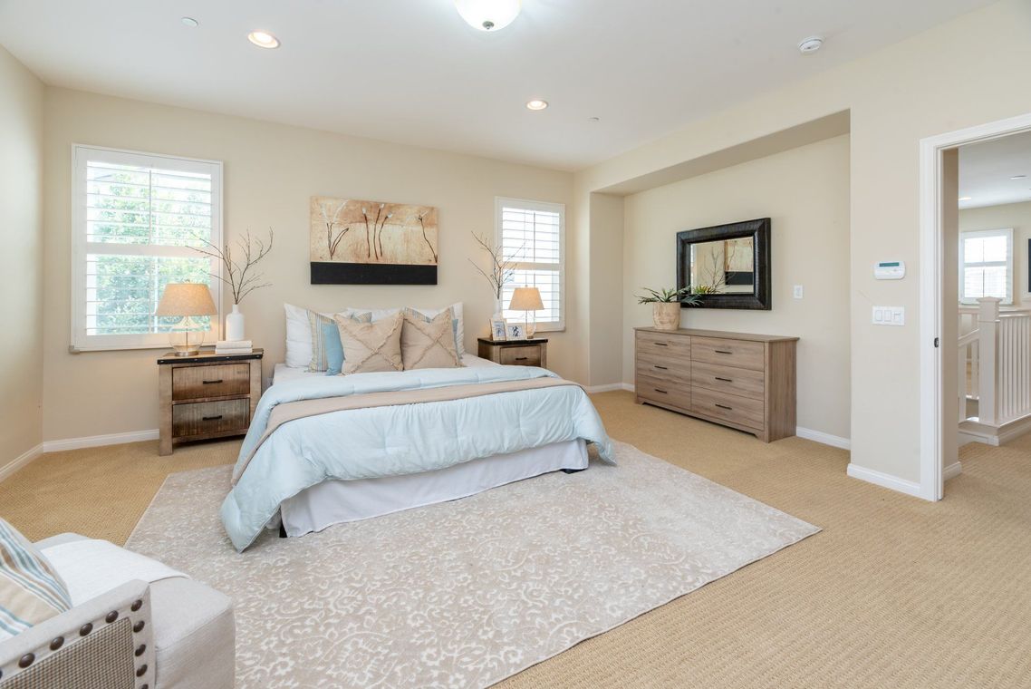 Bright beige bedroom with a king bed, dresser, mirror, and soft carpeted floor