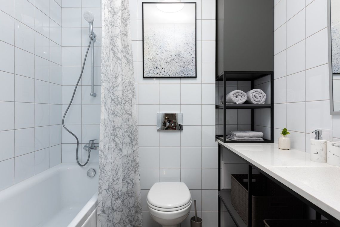 Bright white bathroom with bathtub, toilet, shower curtain, and black shelving beside a sink.