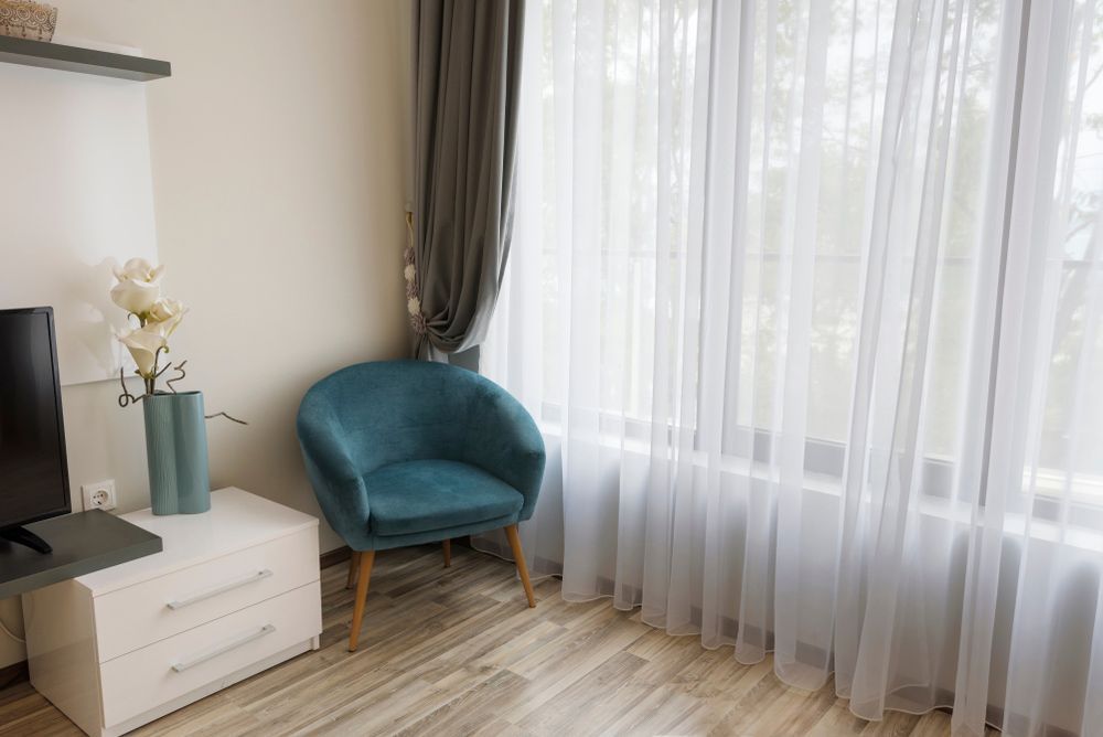 A Living Room With Grey and White Curtains With Dark Green Chair — Curtains in Gold Coast, QLD