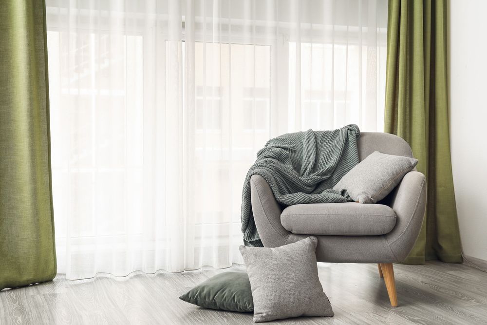 Chair with Blanket and Pillows by Window Adorned with Green Curtains — Window Coverings in Gold Coast, QLD