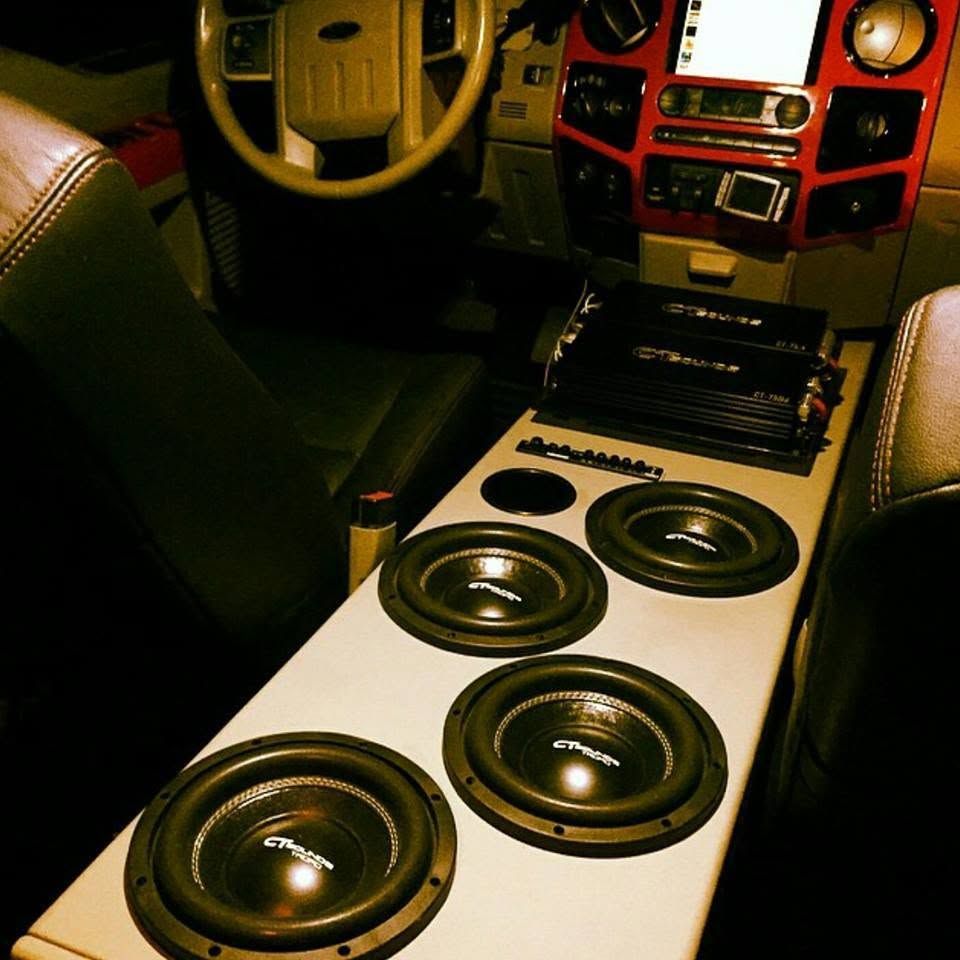 Car interior with four large speakers mounted in the floor and a dashboard stereo display.
