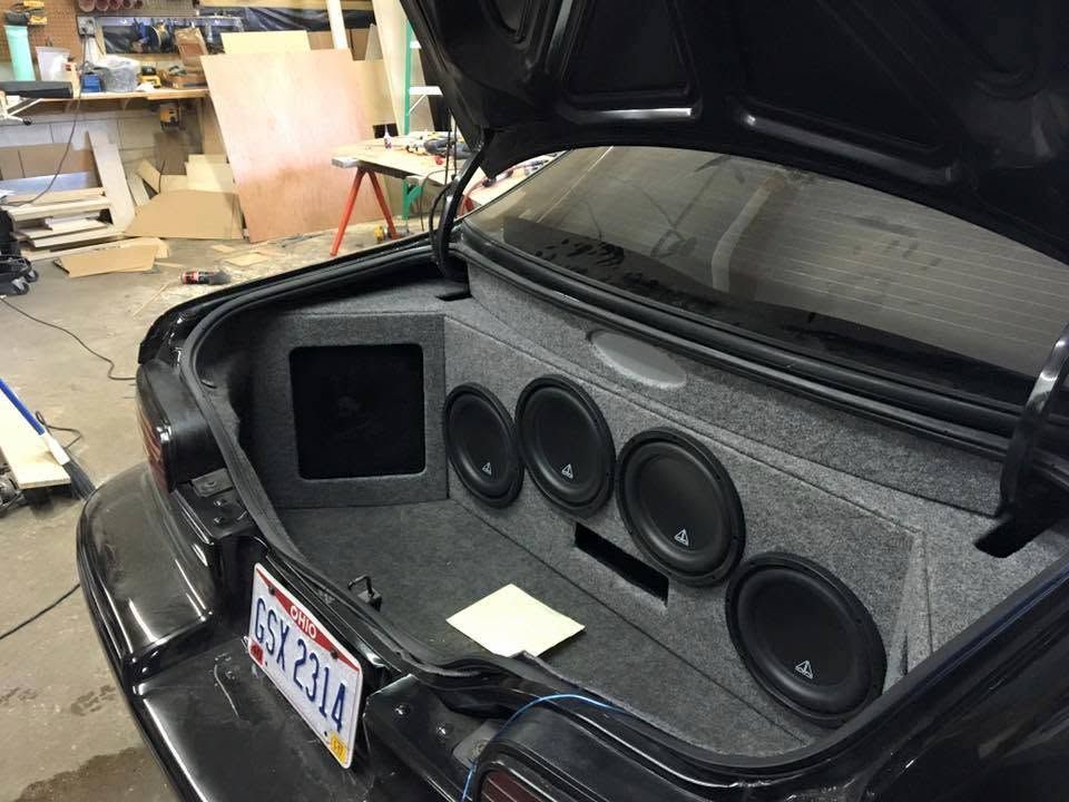 Car trunk with custom speaker/audio setup and carpeted subwoofer enclosure, open in a workshop