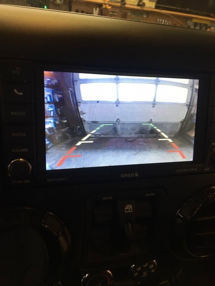Car infotainment screen showing a rearview camera view of a driveway and garage door.