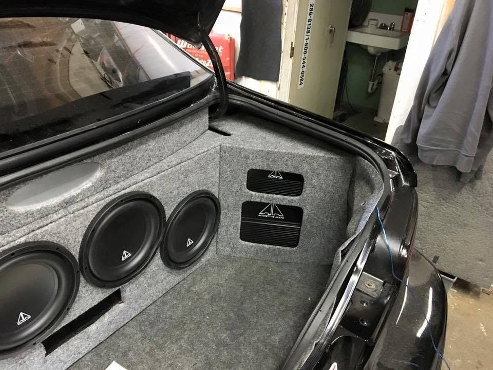Car trunk with custom gray speaker enclosure and multiple black subwoofers installed.