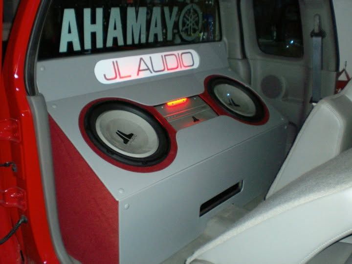 Car audio system with two large speakers and a glowing JL Audio sign in a car trunk