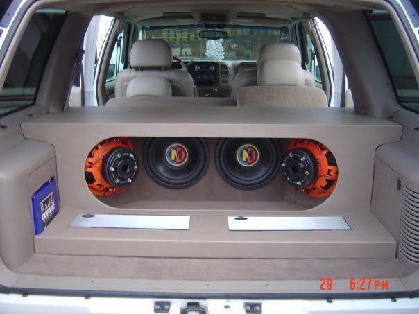 Custom car trunk with large subwoofers and orange speakers installed in a beige interior