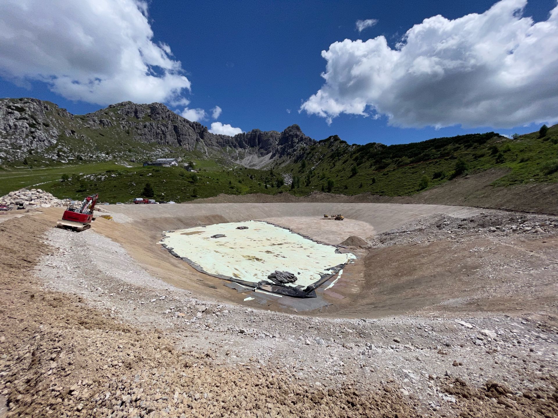 Paesaggio montano roccioso con uno stagno color turchese pallido sotto un cielo nuvoloso e luminoso