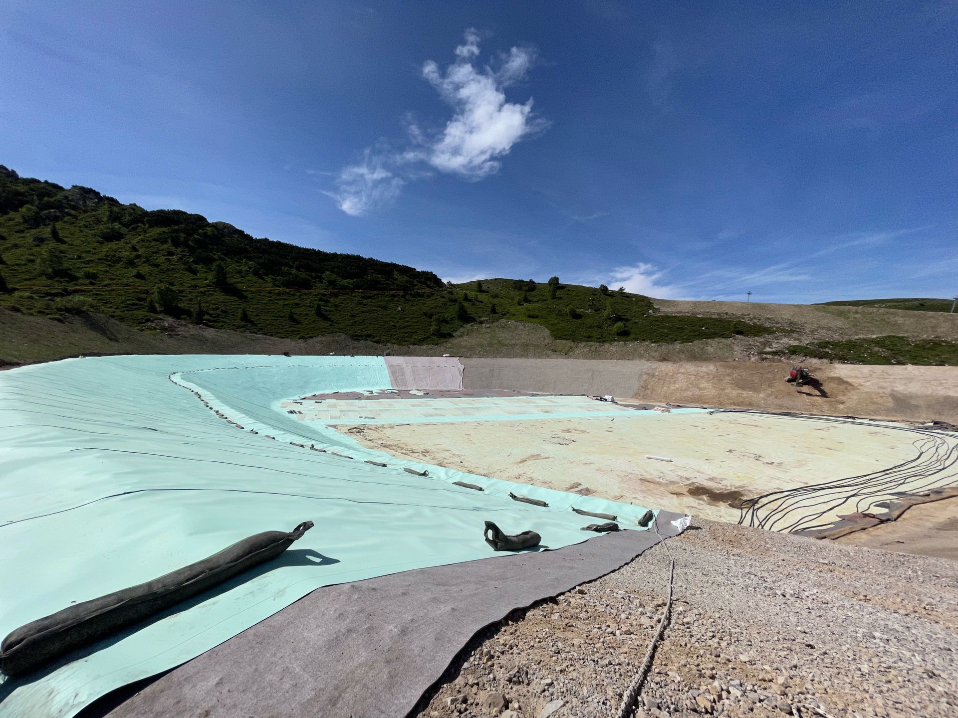 Area lagunare esterna con piscina dalle pareti turchesi, terreno sabbioso e verdi colline sotto un cielo azzurro.