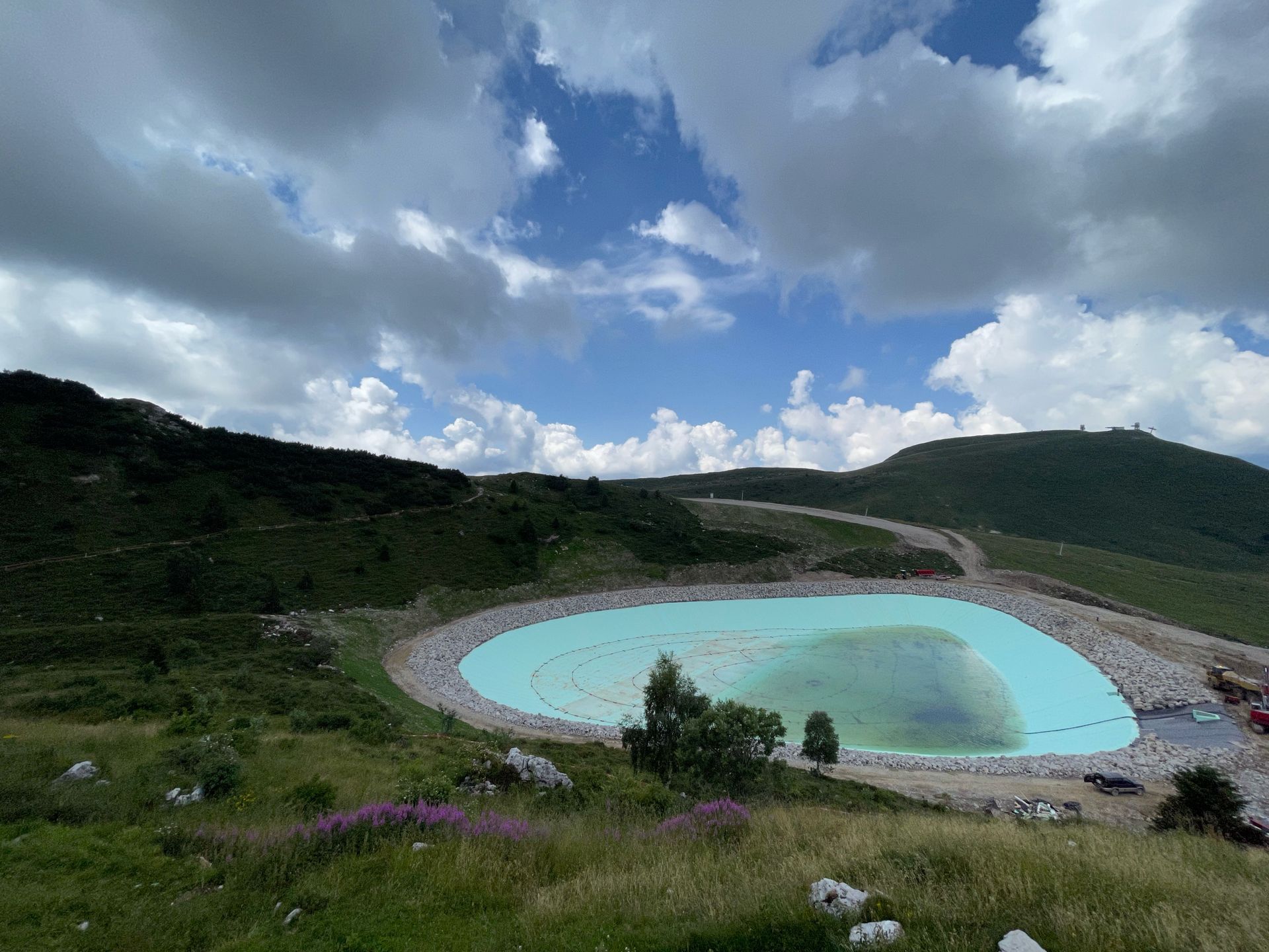 Laguna turchese in un cratere vulcanico sotto un cielo nuvoloso, circondata da verdi colline e da una strada tortuosa