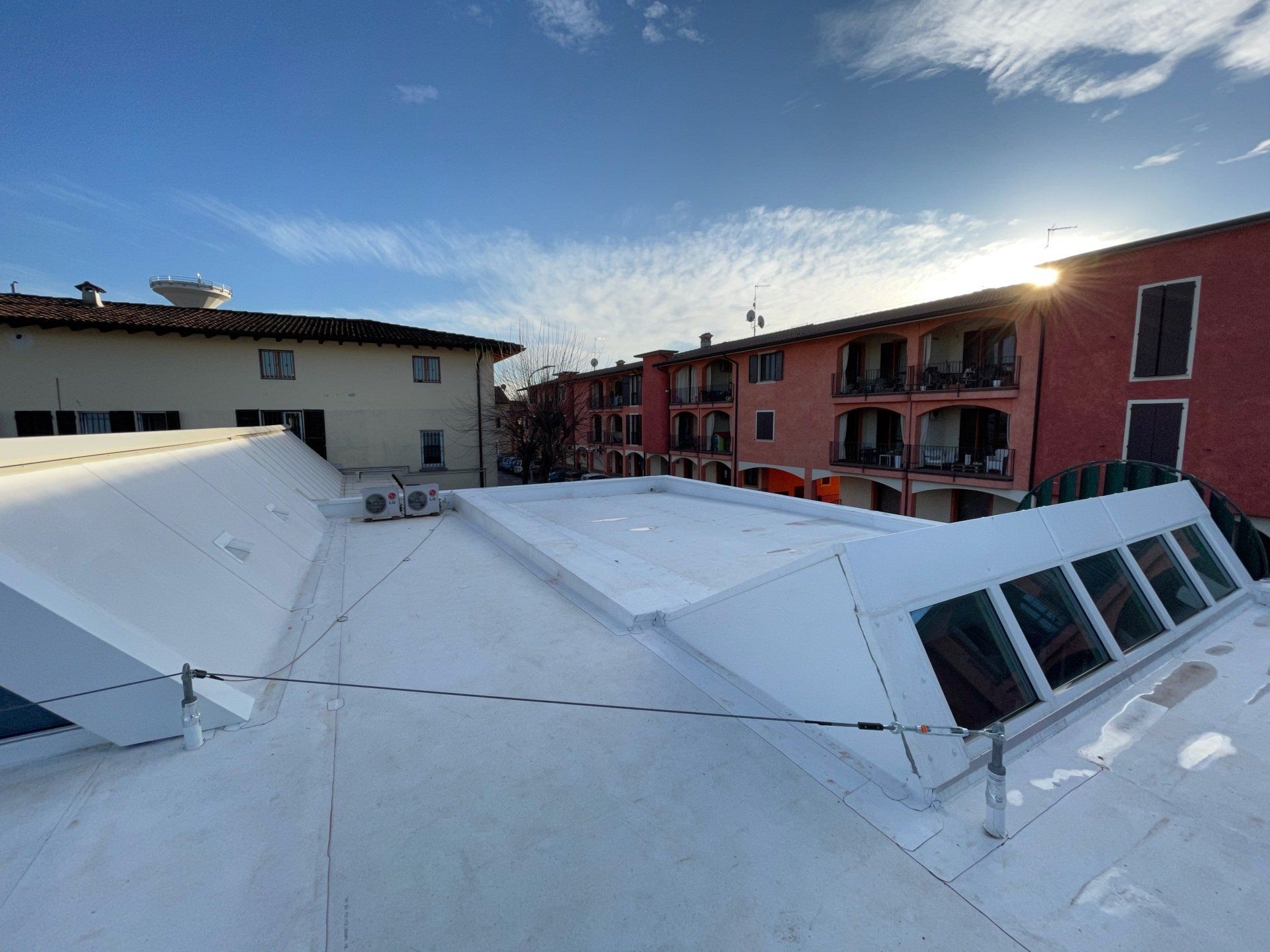 Tetto innevato con lucernari, fiancheggiato da palazzi residenziali sotto un cielo limpido.