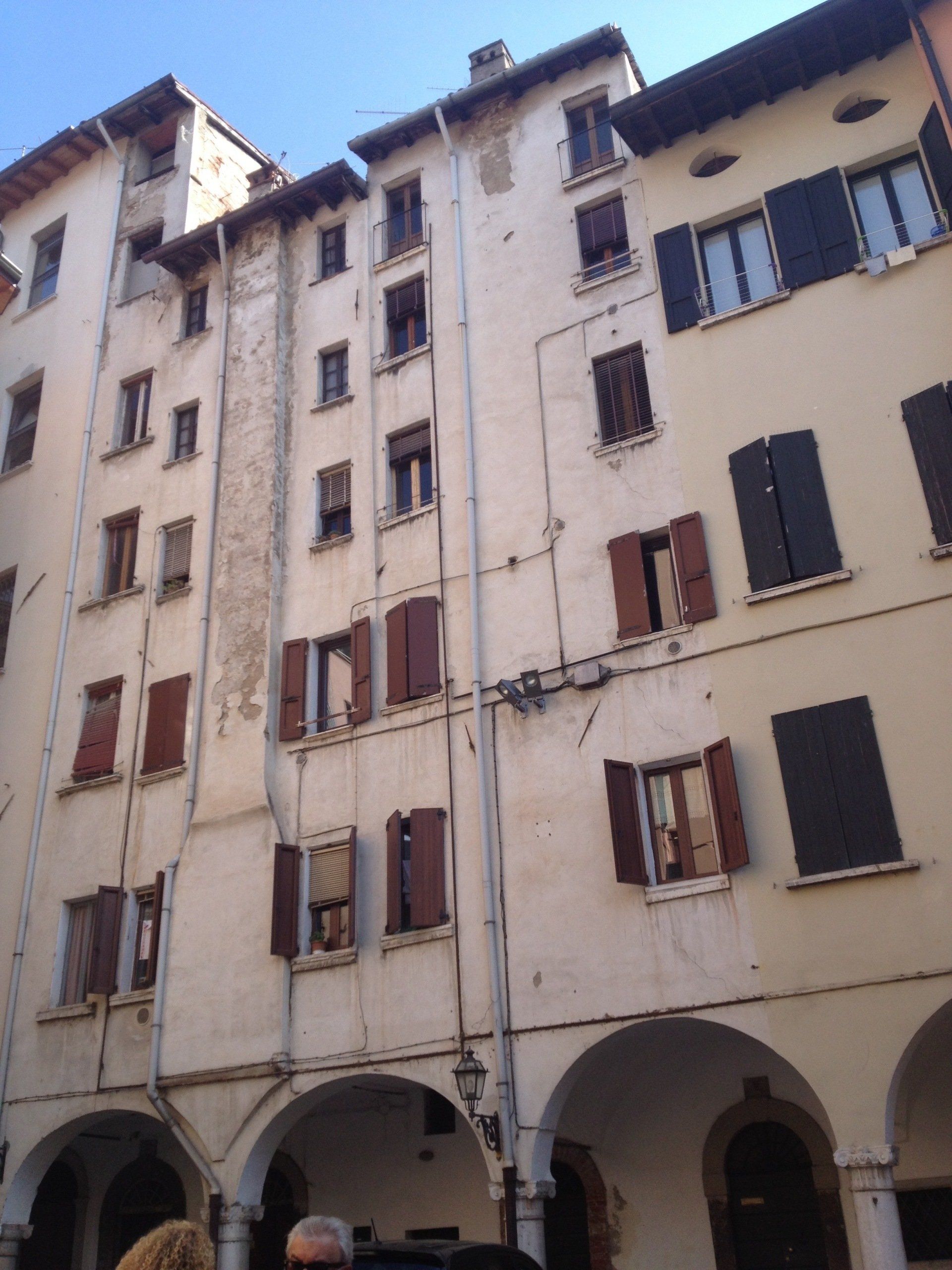 Vecchio palazzo residenziale in stile europeo con facciate color crema, finestre con persiane e portici ad arco al piano terra.