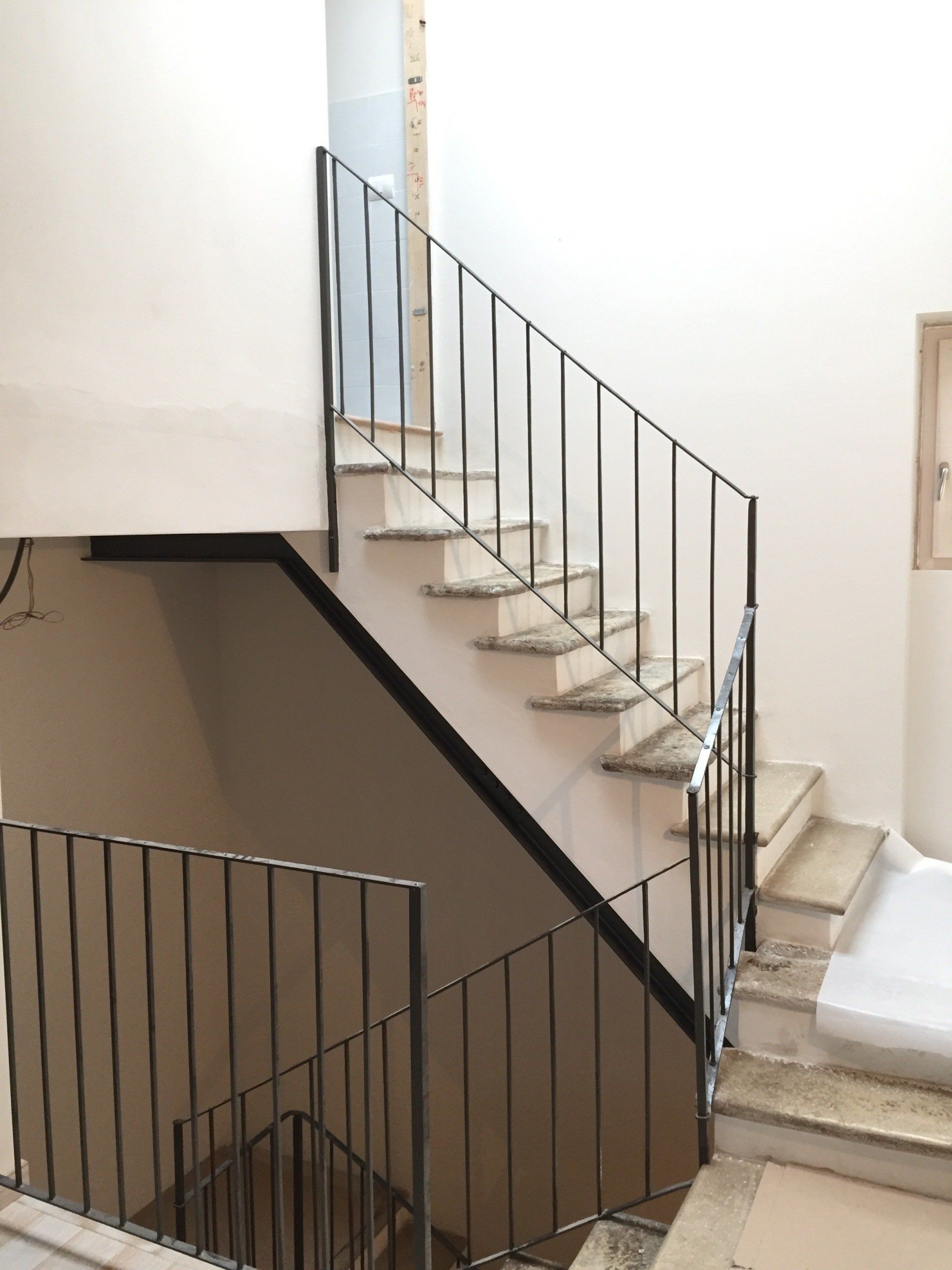 Scala interna con pareti bianche, ringhiere scure e pianerottolo in uno stretto vano scale.